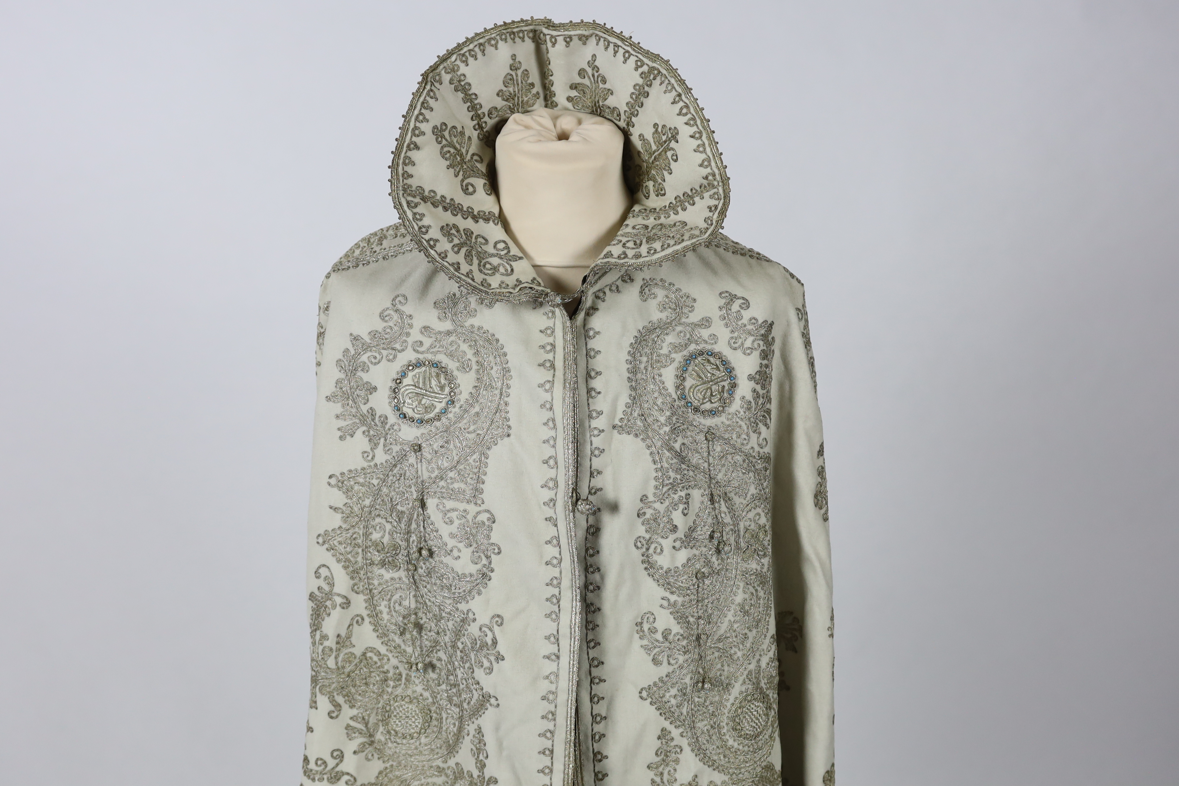 A 19th century Indian fine cream wool embroidered cape, probably made for the European market, embroidered in panels of silver metallic thread in an ornate vertical design with turquoise embellishments and lined in black